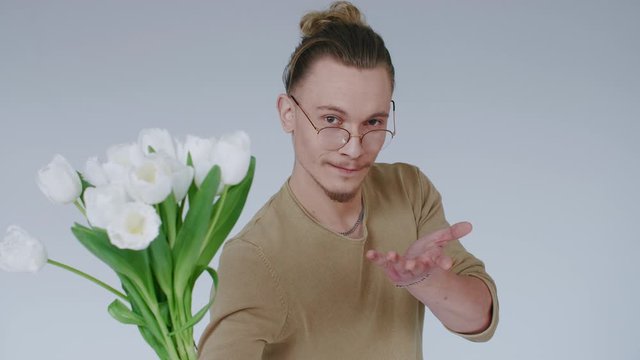 Young handsome man, lovelace flirts, gives flower bouquet, looks at camera