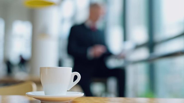 Coffee cup standing on the office desk in front view with a blurred image of businessman working on background. Morning coffe video in office.