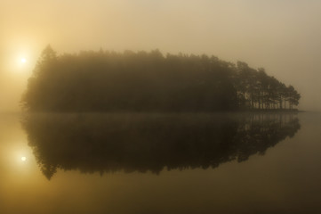 Obraz na płótnie Canvas Sun shining through fog and trees on island in Finnsjön, Mölnlycke, Sweden