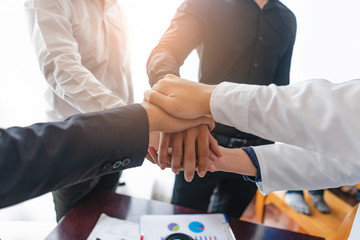 Fototapeta premium professionals putting hands together piling on top of one another, businessmen, doctors, architectures, engineer and colleagues, standing around table with money, glasses, and blueprint on the table