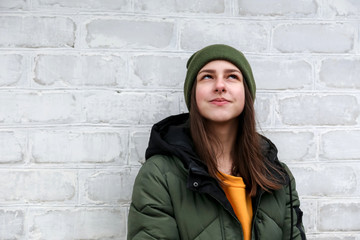 Portrait of a beautiful pensive girl in a yellow sweater and khaki hat, which stands near a white brick wall. The concept of emotions and copy space