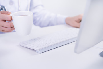 Business concept - Young female doctor woman working at office with computer, typing electronic medical record, white table background, close up, copy space