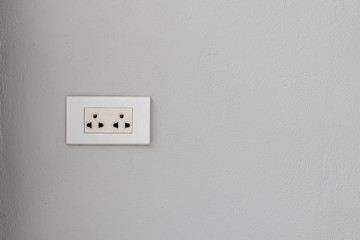 The white electrical plug socket  on a gray concrete wall.