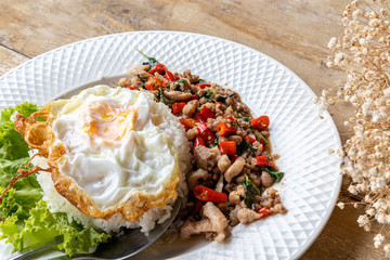 Stir fried minced pork basil with steamed rice and fried egg on a white plate.