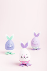 Funny cute bunny eggs in pastel colors on pink table top, Easter holiday concept. Easter decoration for kids still life, copy space
