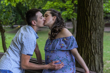 Young couple in love husband and pregnant wife kiss in the park, happy family