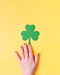 Woman holding shamrock symbol for Saint Patrick's Day on bright yellow background. Minimalistic...