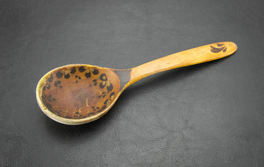 Old shabby wooden spoon handmade brown. Vintage patterned scratched food accessory on a black leather background.