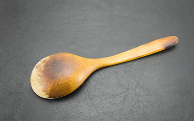 Old shabby wooden spoon handmade brown. Vintage patterned scratched food accessory on a black...