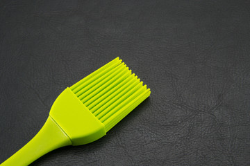 The kitchen brush is silicone, light green in color. Plastic accessories for the kitchen, cooking and coating. Black leather background.