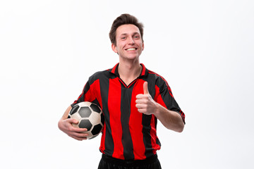 Excited soccer player in a red sportswear showing thumb up holding soccer ball. © ianachyrva