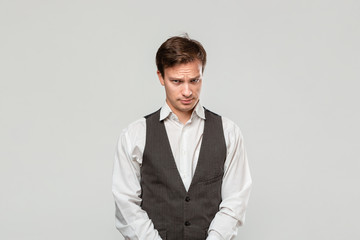Young man in a white shirt and grey vest in high dudgeon over grey background