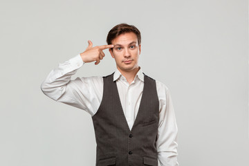 Young man in a white shirt and grey vest pointing with finger at the head