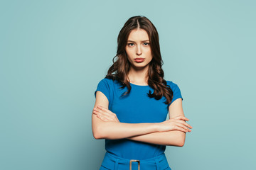 Obraz premium serious, attractive girl looking at camera while standing with crossed arms on blue background