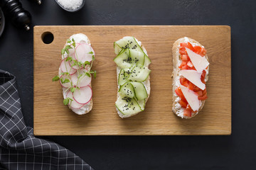 Different sandwiches on toast with vegetables, radishes, tomatoes, cucumbers and microgreens on black. View from above.