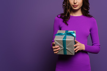 cropped view of young woman holding gift box on purple background