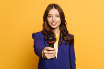 selective focus of journalist holding microphone on yellow background