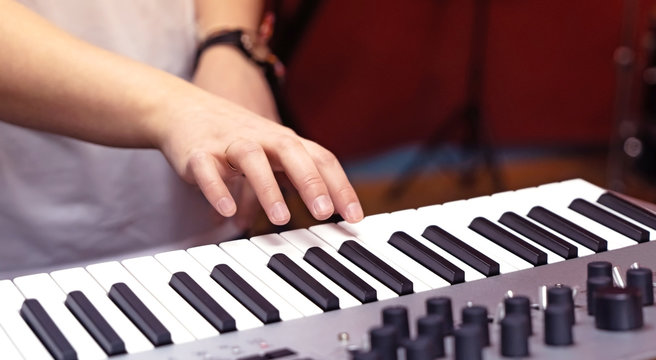 Electronic synthesizer and part of a woman's hand in close-up.