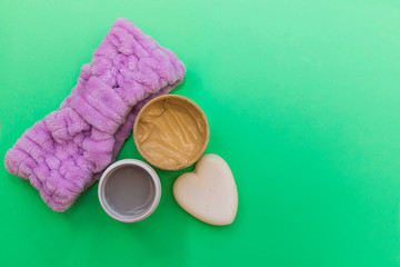 Purple headband, cosmetic cream, scrub and heart-shaped soap flat lay