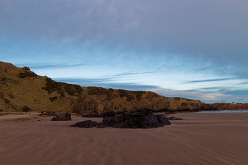 Fototapeta premium The North end of St Cyrus beach with the tide out and the Boulders exposed from the wet red sand under darkening skies.