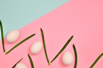 White eggs with green myrtle leaves pattern on mint and pink trendy color background. Spring and Easter holiday concept with copy space.