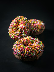 three glazed Donut with colorful sprinkles isolated on black background. angel view.