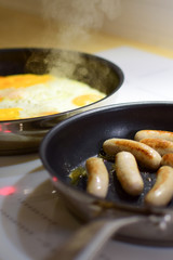 Cooking on an induction cooker. Fried eggs and sausages in pans.