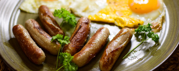 Fried Bavarian sausages and fried eggs are served on a ceramic plate.