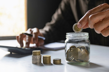 Men are saint documents about save money and put coin in glass jar on desk on table in the office.