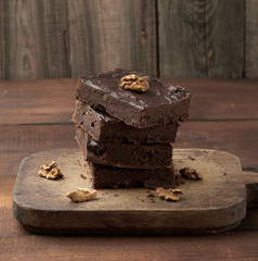 stack of square baked slices of brownie chocolate cake with walnuts on a wooden surface