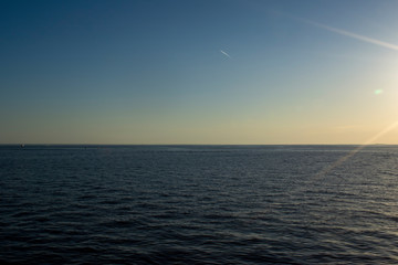 view of the sea surface and cloudless sky in the rays of the sun at sunset