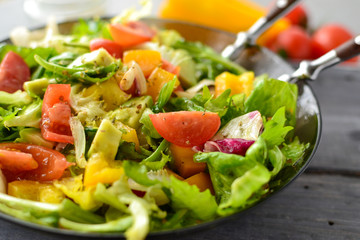 Vegan Spring Salad. Tomato, lettuce, dressing, bell peppers and avocados. Vegetable  summer salad in a plate with a fork, close-up