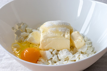 Cottage cheese, butter, egg and sugar in a white bowl - ingredients prepared for mixing. The process of making curd bagels or croissants