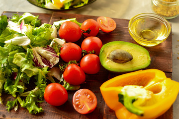 Ingredients for vegan spring and summer salad. Vegetables on a cutting board. Tomatoes, sweet yellow pepper, lettuce, dressing, avocado, oil in a bowl.