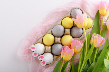 Easter composition of eggs, tulips and rabbit paws in cardboard box on white background