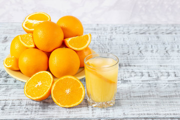 Glass of orange juice and a plate with oranges on a wooden table. Freshly squeezed orange juice.