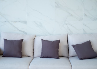 Gray color pillow on white sofa of white marble wall.
