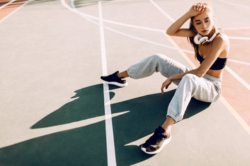 Attractive tired athletic young woman outdoors posing sitting on basketball court