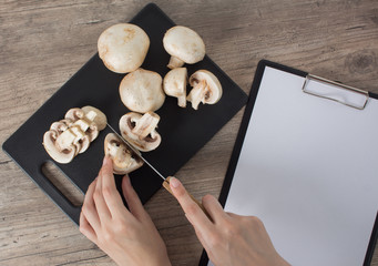 Food. To cook the champignon. Cut mushrooms with a knife on a black cutting Board. Write down the recipe. Copy space, clear space. Tablet with a blank sheet of paper. Vegan, vegetarian.