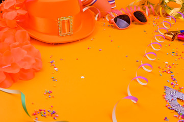 Decor for a traditional celebration of King's Day in the Netherlands. Orange hat, glasses, jewelry and confetti on a bright background. Picture in the form of a frame. Copy space. Horizontal format