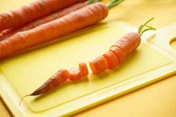 Freshly sliced carrots in slices on a yellow cutting kitchen board, on a yellow background