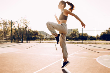 Fototapeta na wymiar Attractive young girl sportswoman training outdoors, wearing headphones, doing jumps