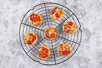 Small pizzas topped with cheese, tomato, yellow and red bell peppers and salami sausage on round black grid, top view