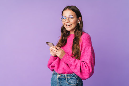 Image of young woman wearing earbuds smiling and holding cellphone