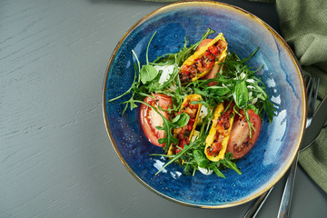 Close up view on Appetizing Italian caprese salad with fresh tomatoes, soft mozzarella, arugula and sauce in blue bowl rustic background. Top view, copy space, flat lay