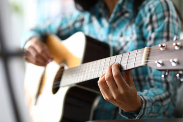 Skillful musician fingers on guitar fretboard. Woman plays chords on acoustic guitar, in her other hand convenient pick. Student performs exercises on instrument to improve abilities