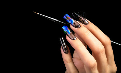 Hand with a beautiful manicure and a brush on a black background. Nail design. Extended nails.