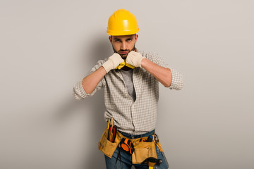 handsome workman in hardhat and gloves with tool belt on grey