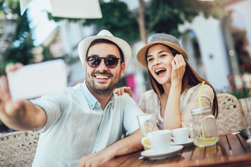 Beautiful loving couple sitting in a cafe enjoying in coffee and using phone, make selfie photo.
