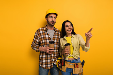 smiling manual workers with coffee to go pointing on yellow
